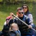 A family of four rowing a canoe on a serene lake during a sunny day, enjoying an outdoor adventure.